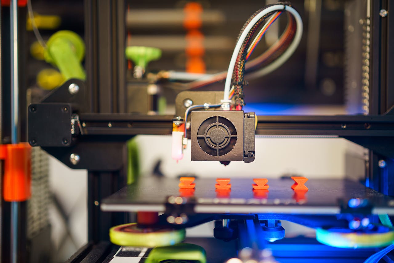 portfolio-03 Detailed view of a 3D printer in action, fabricating small plastic pieces indoors.
