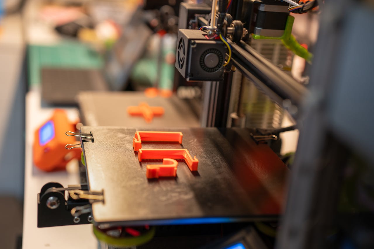portfolio-07 Detailed view of a 3D printer creating an orange plastic part showcasing advanced technology.