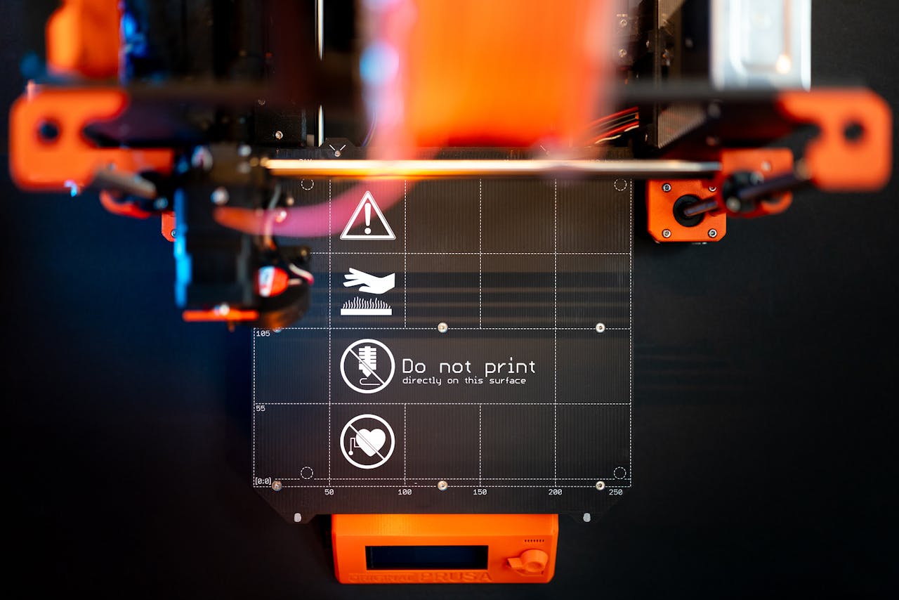 portfolio-01 Detailed image of a 3D printer with caution signage, showcasing advanced manufacturing.