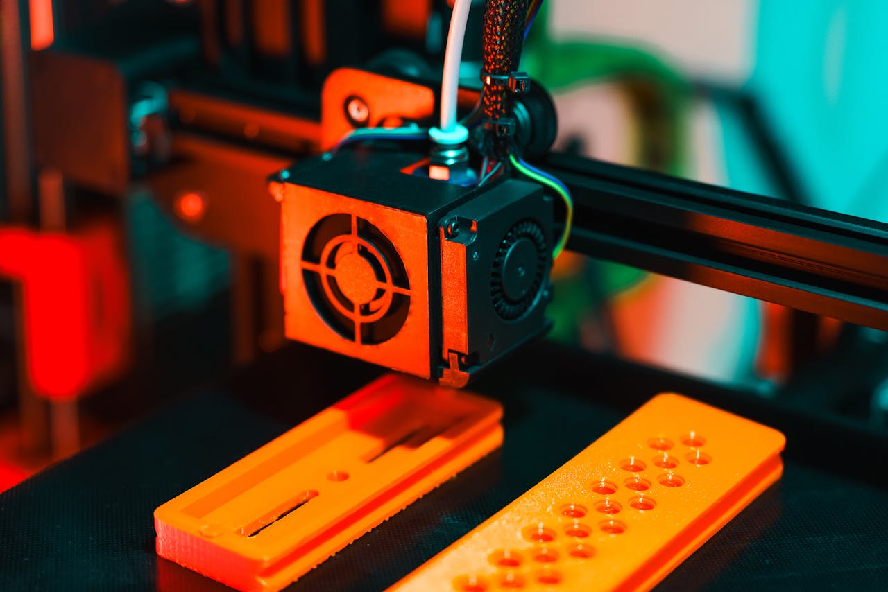 portfolio-06 Detailed view of a 3D printer in action, extruding orange plastic components.